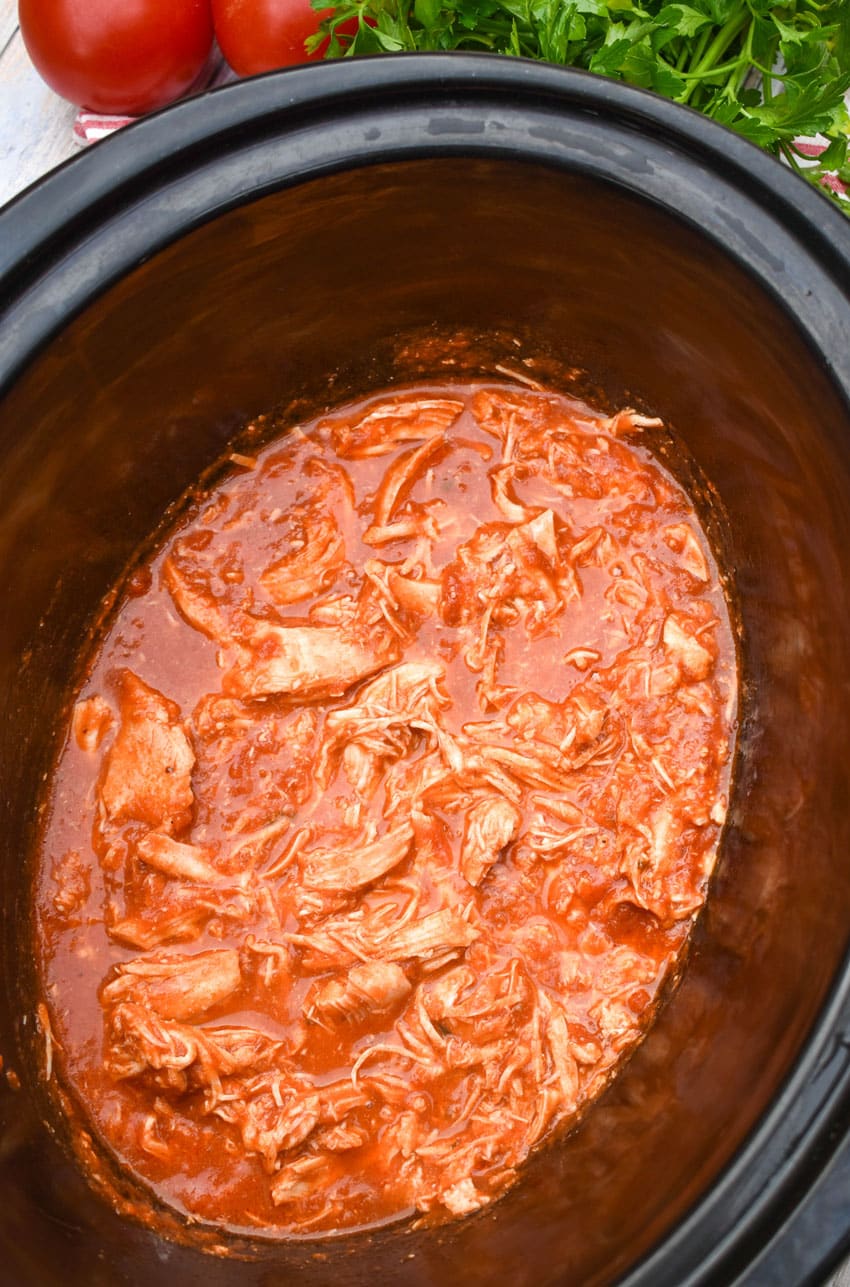 shredded chicken in red sauce in the black bowl of a slow cooker