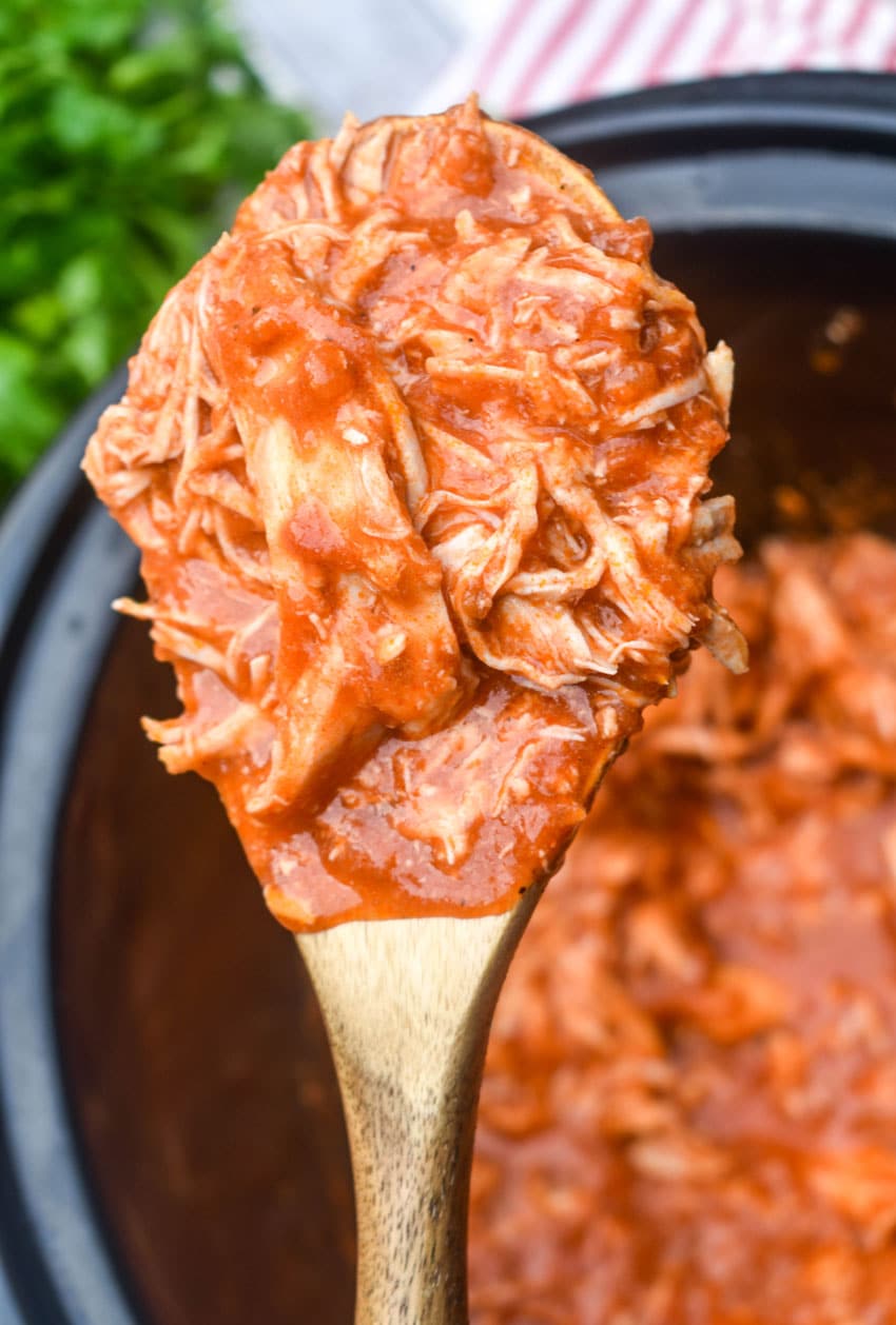 a wooden spoon holding up a scoop of slow cooker shredded parmesan chicken