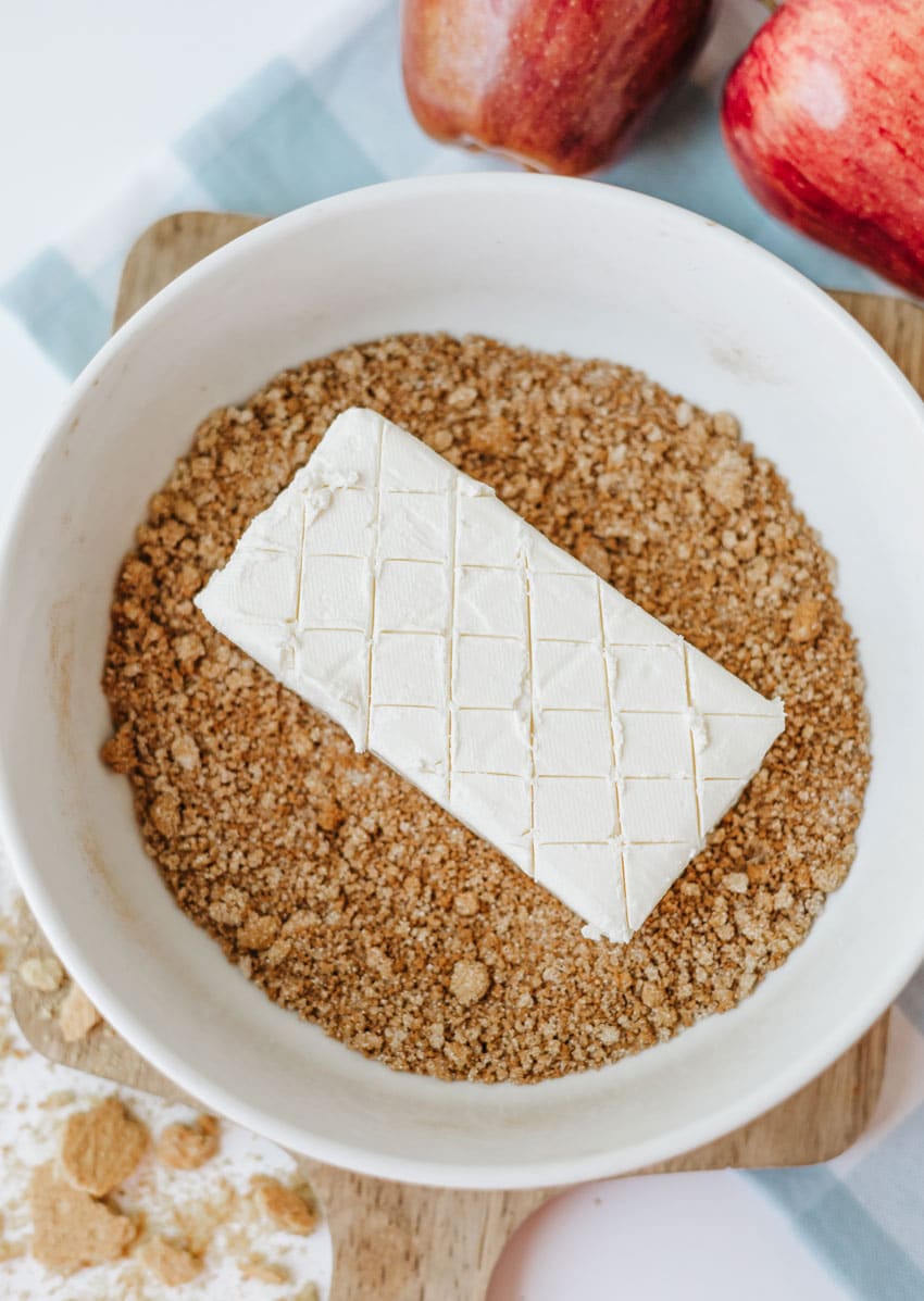 a scored bar of cream cheese in a bowl of spiced cracker crumbs