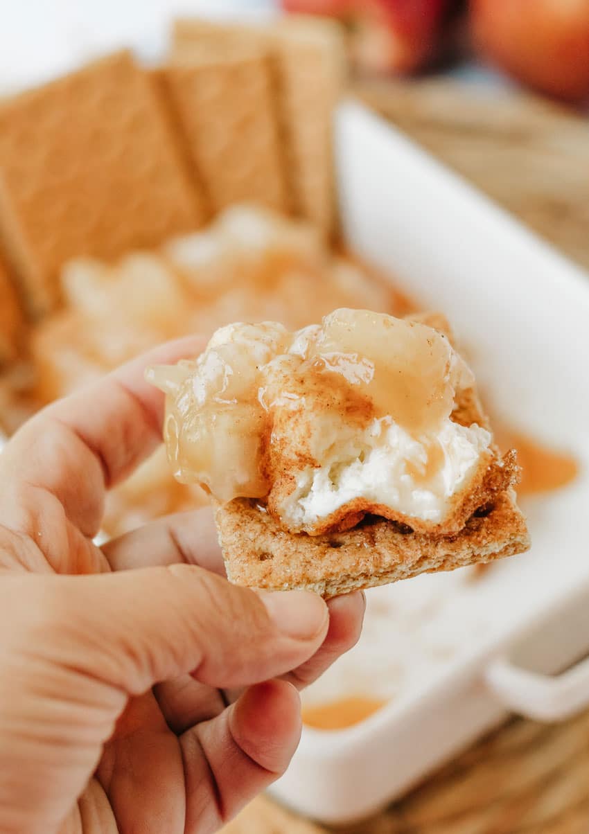 a hand holding up an apple pie smoked cream cheese topped graham cracker square