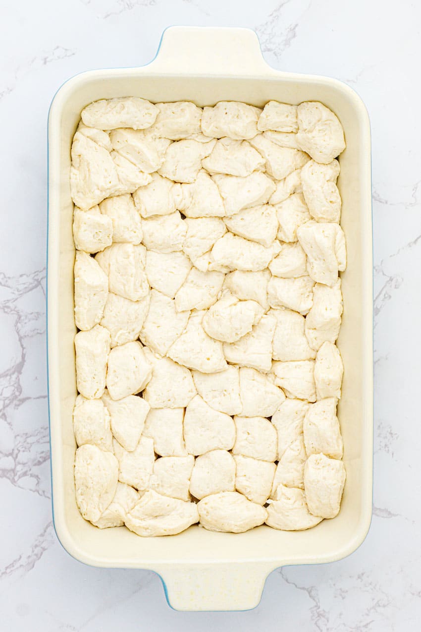 refrigerated biscuit pieces spread in an even layer in a white casserole dish