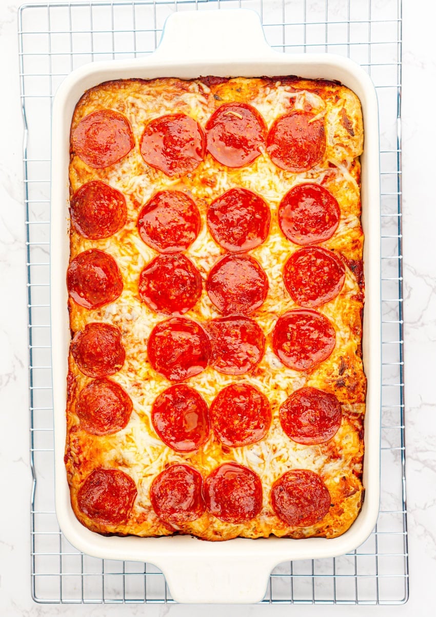 a baked bubble up pizza casserole in a white baking dish on a wire rack