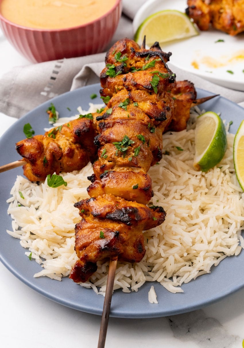 two chicken satay skewers over steamed white rice on a blue plate
