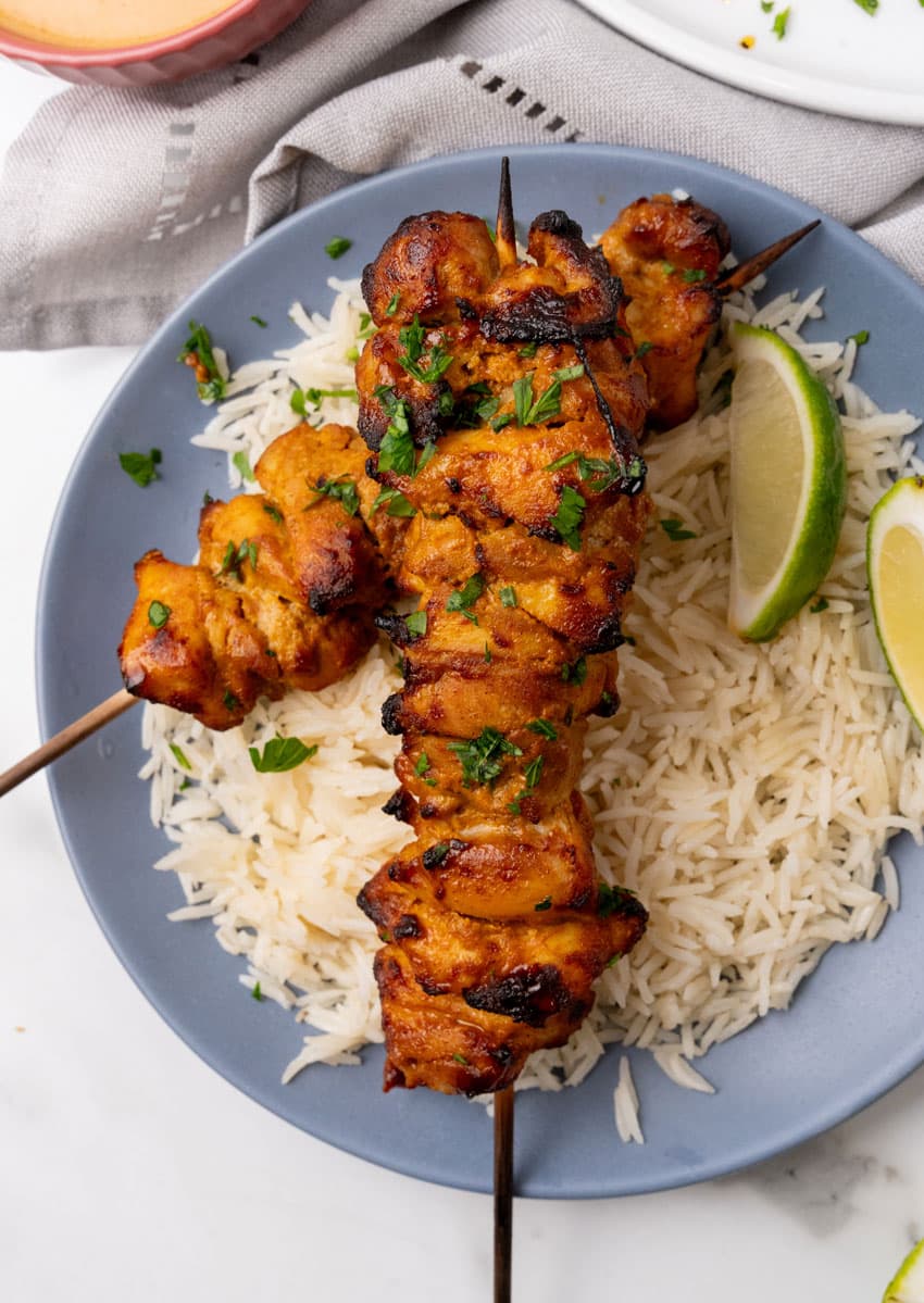 two chicken satay skewers over steamed white rice on a blue plate