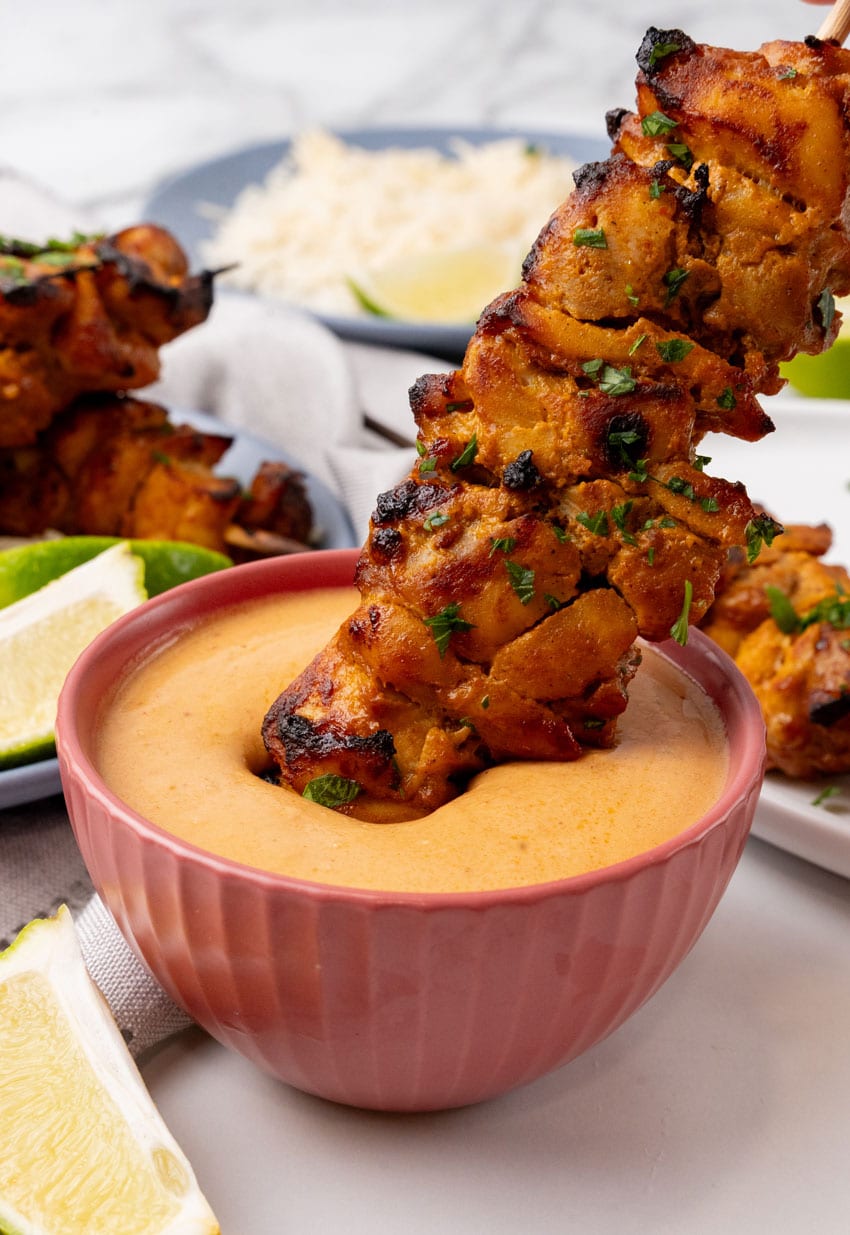 a chicken satay skewer being dipped in a small bowl of creamy homemade peanut sauce
