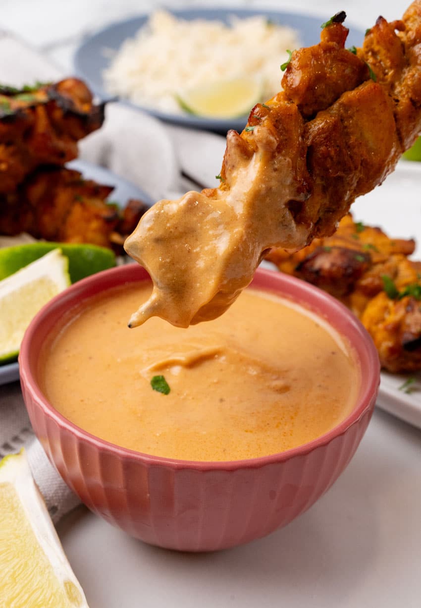 a chicken satay skewer dipped in creamy homemade peanut sauce