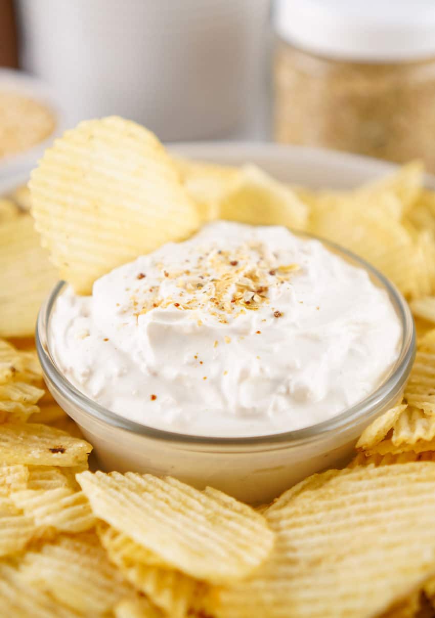 homemade french onion dip in a small glass jar surrounded by potato chips