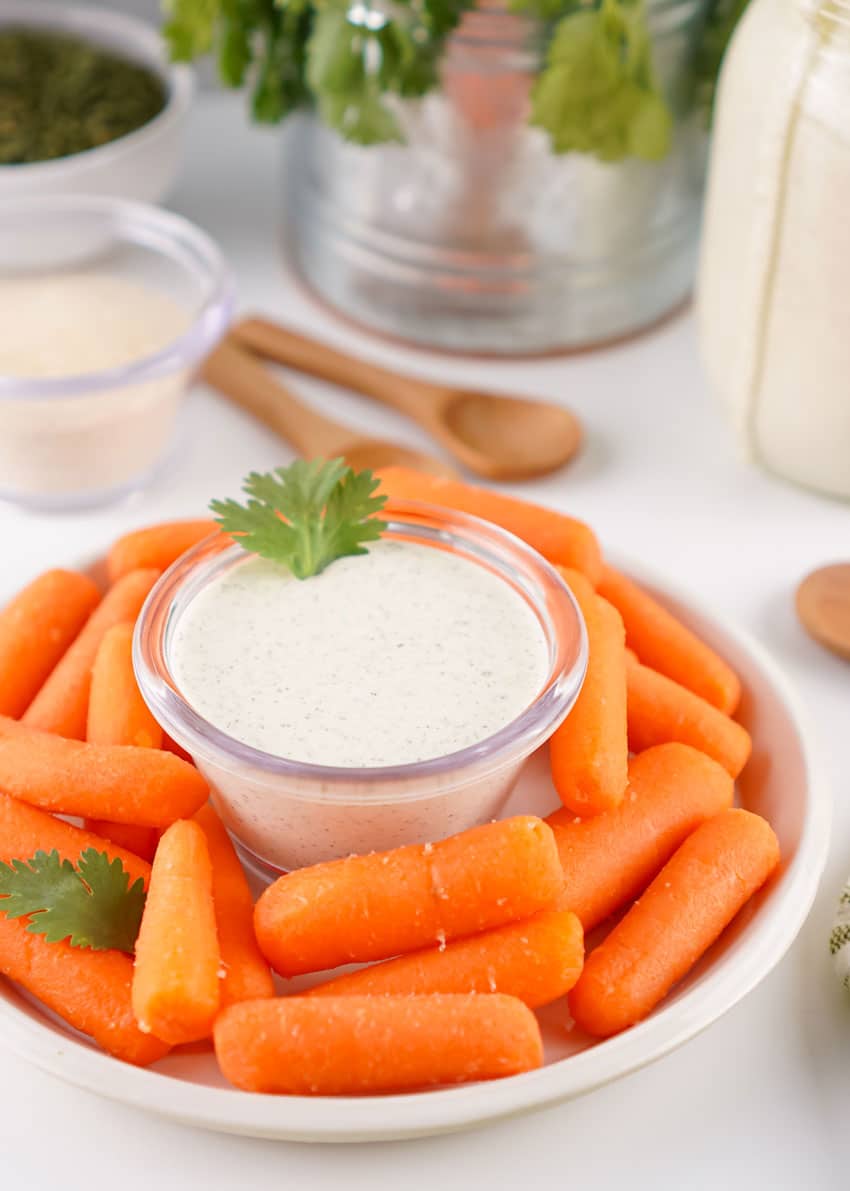 homemade ranch dressing in a small glass jar surrounded by baby carrots