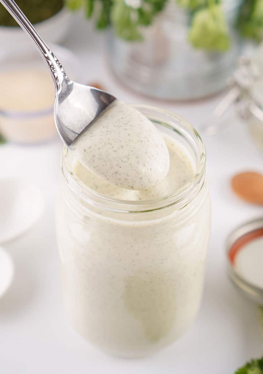 a silver spoon scooping homemade ranch dressing out of a glass jar