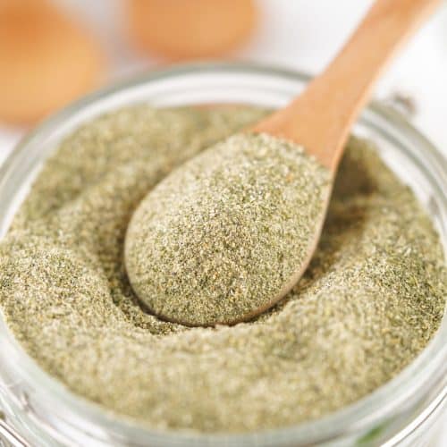 a wooden spoon scooping homemade ranch seasoning mix out of a small glass jar