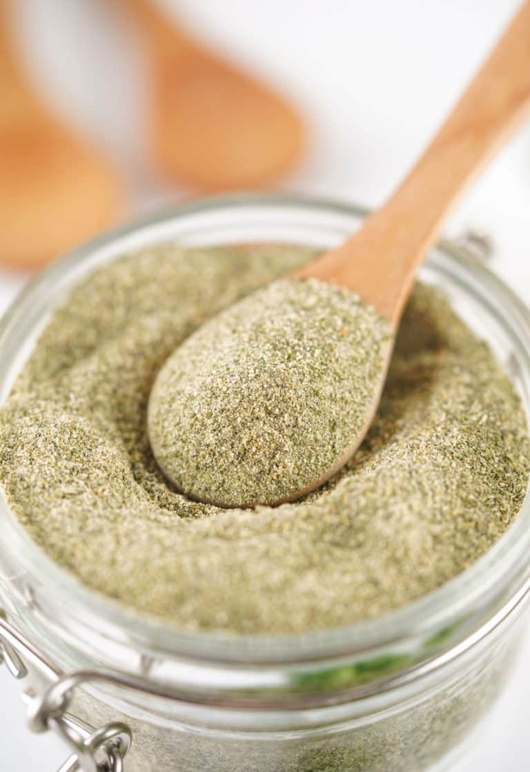 a wooden spoon scooping homemade ranch seasoning mix out of a small glass jar