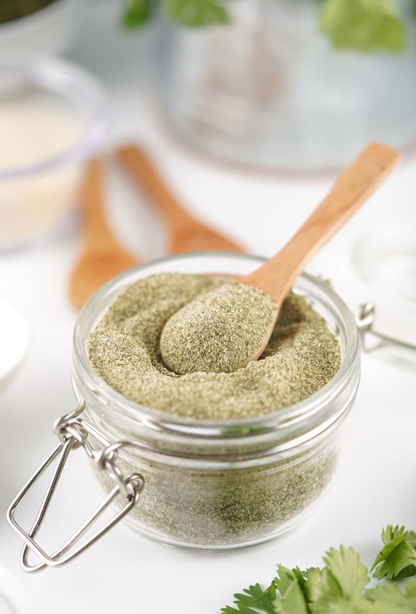 a wooden spoon scooping homemade ranch seasoning mix out of a small glass jar
