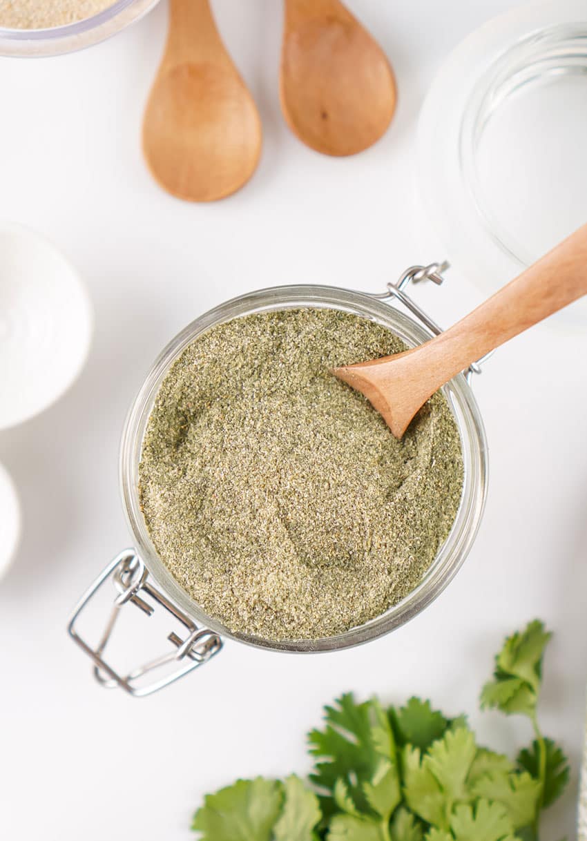 a wooden spoon scooping homemade ranch seasoning mix out of a small glass jar
