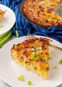 a slice of ham and cheese hash brown quiche on a white plate