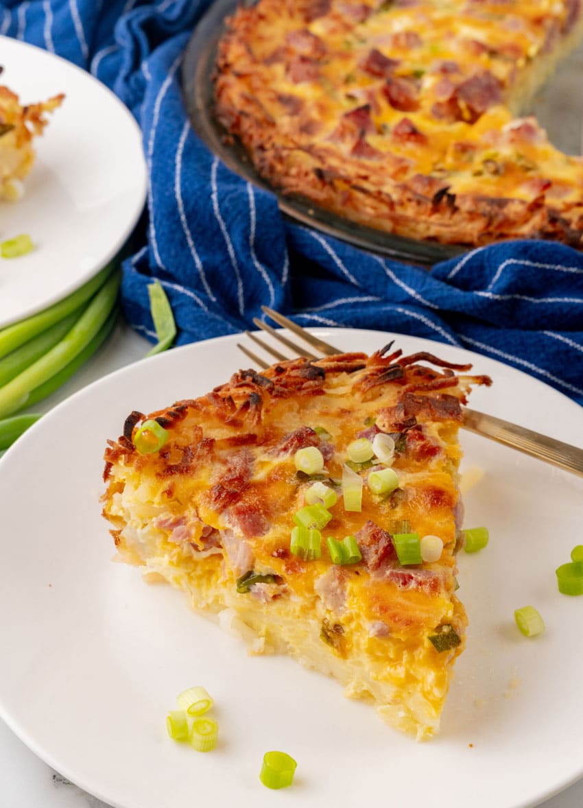 a slice of ham and cheese hash brown quiche on a white plate