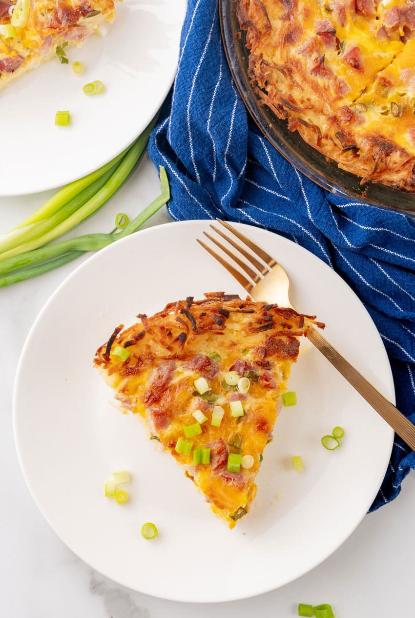 a slice of ham and cheese hash brown quiche on a white plate