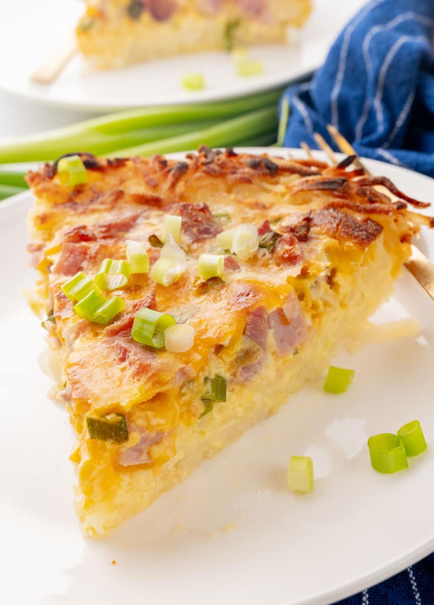 a slice of ham and cheese hash brown quiche on a white plate
