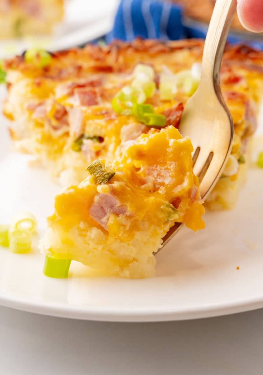 a slice of ham and cheese hash brown quiche on a white plate