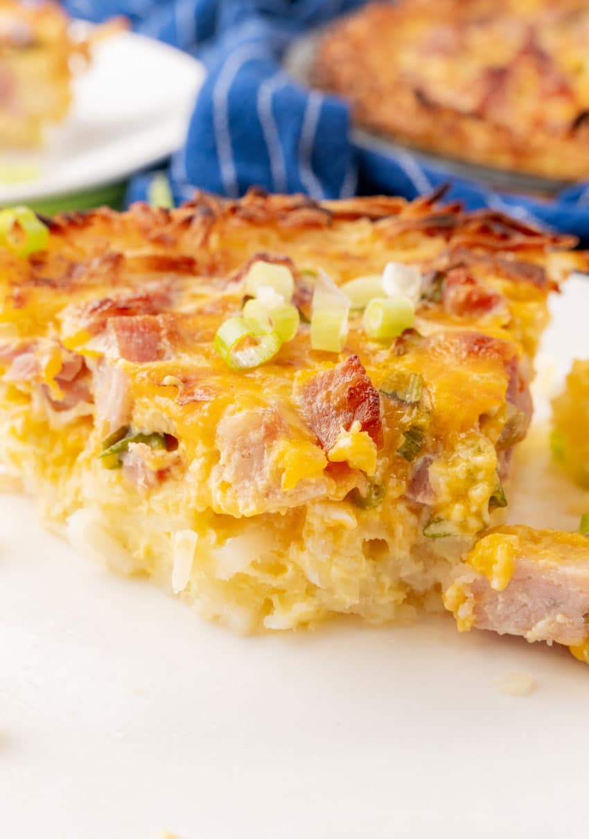a slice of ham and cheese hash brown quiche on a white plate