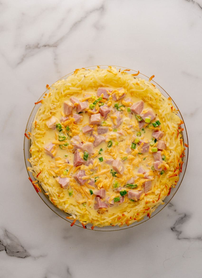an unbaked ham and cheese hashbrown quiche in a glass pie plate