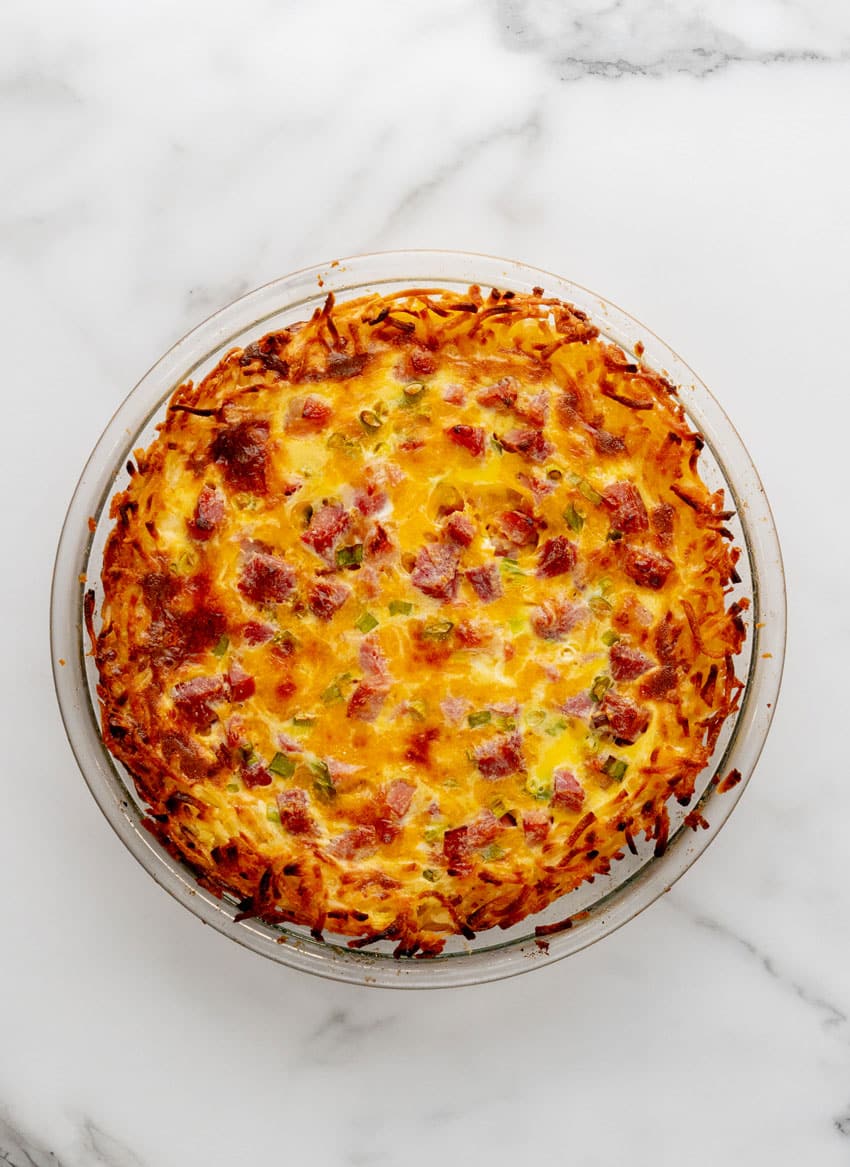 a baked ham and cheese hash brown quiche in a glass pie dish