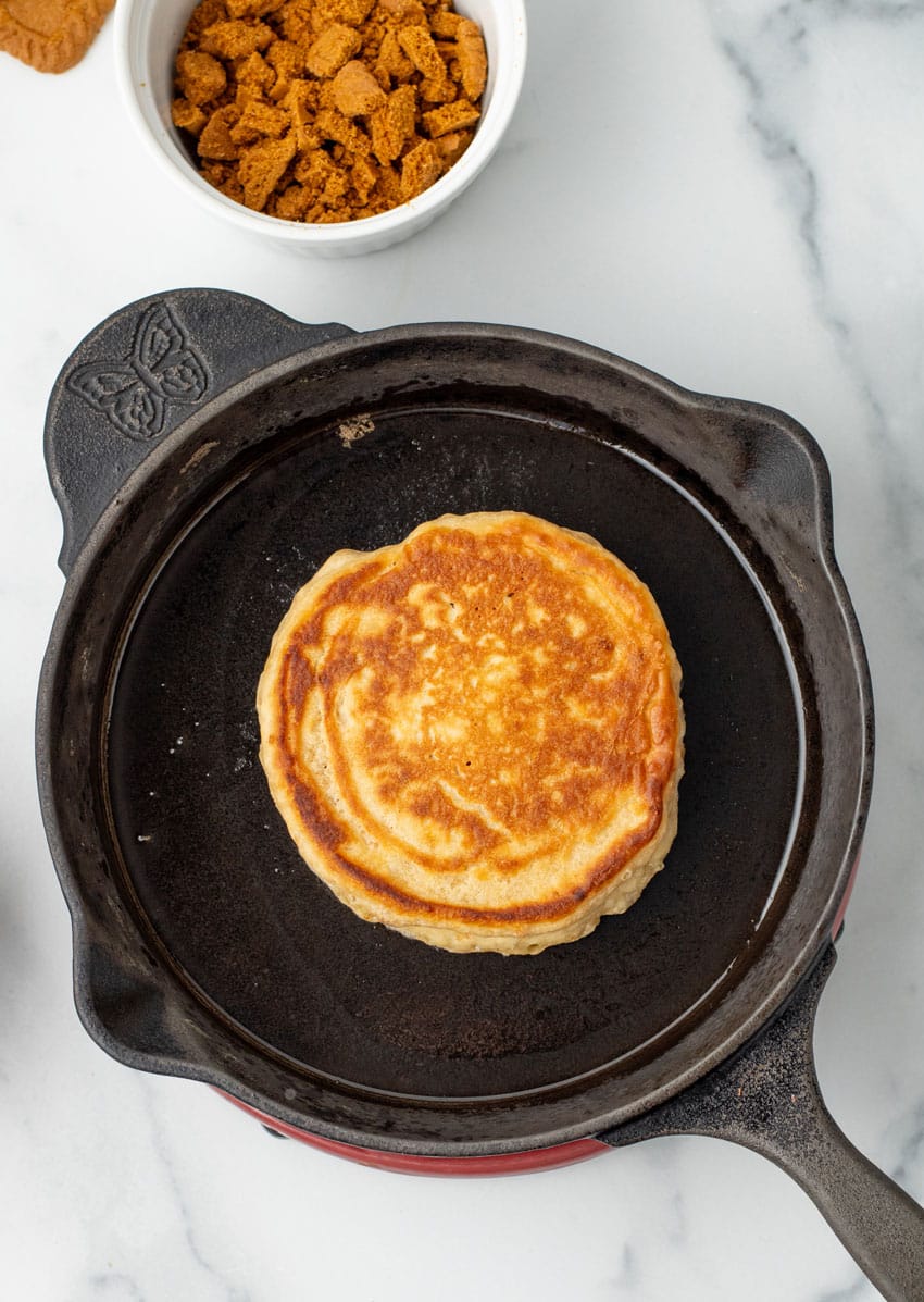 a cookie butter pancake frying in a large cast iron skillet
