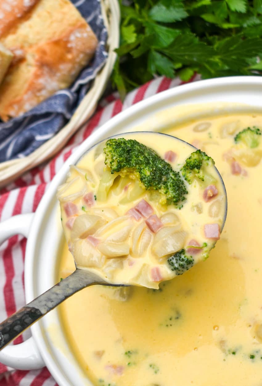 a silver ladle holding up a scoop of boxed macaroni and cheese soup with ham and broccoli