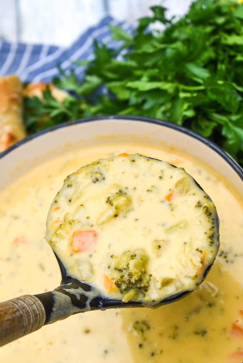 a black ladle holding up a scoop of homemade broccoli cheddar soup