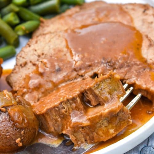 a fork scooping a piece of gravy topped slow cooker eye of round roast off a white plate