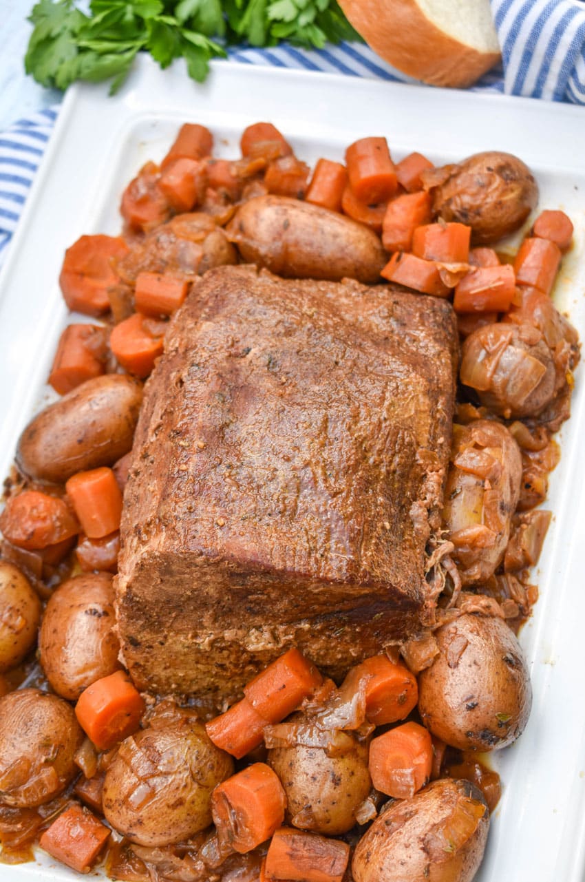 slow cooker eye of round roast surrounded by cooked carrots and potatoes on a white serving platter