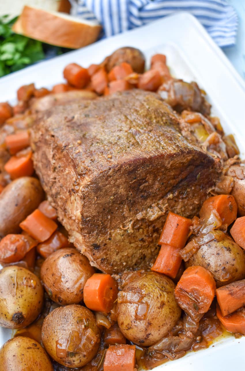 slow cooker eye of round roast surrounded by cooked carrots and potatoes on a white serving platter