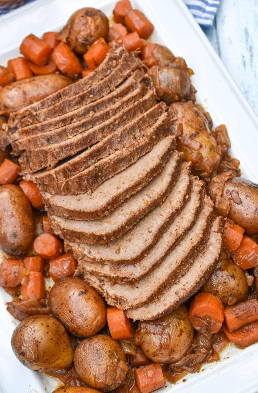 slices of slow cooker eye of round roast surrounded by cooked carrots and potatoes on a white serving platter