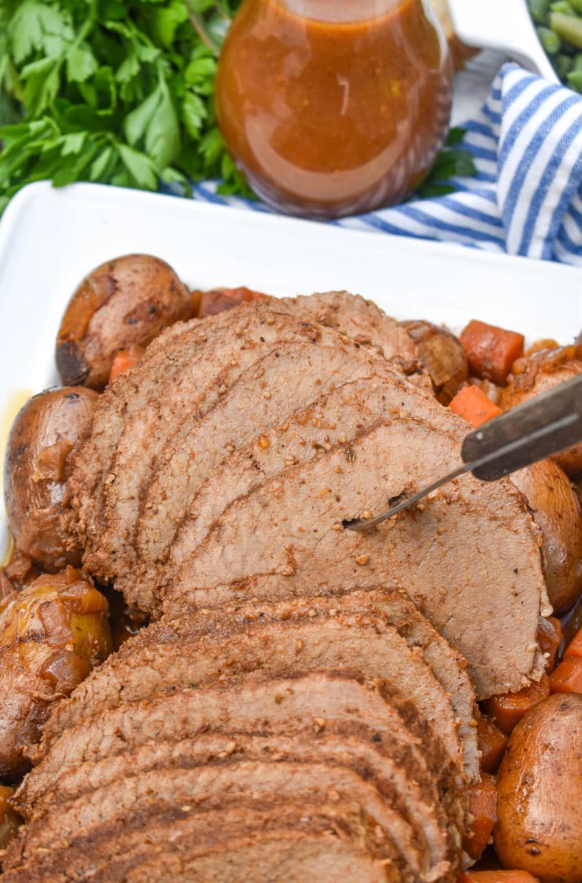 slices of slow cooker eye of round roast surrounded by cooked carrots and potatoes on a white serving platter