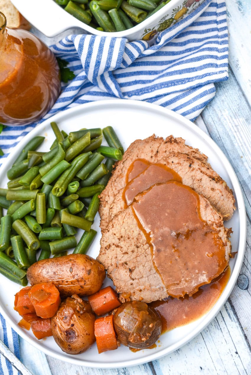gravy covered slices of slow cooker eye of round roast on a white plate