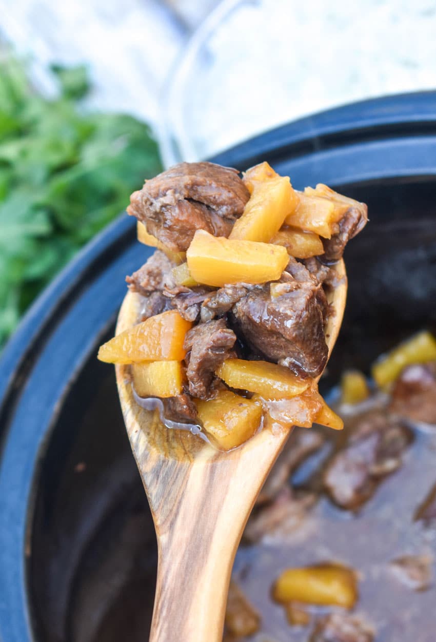 a wooden spoon holding up a scoop of crockpot steak teriyaki