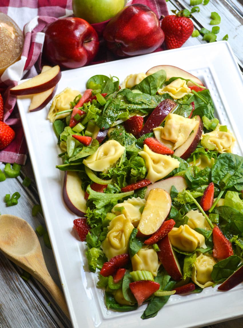 spinach tortellini salad with strawberries on a white serving platter