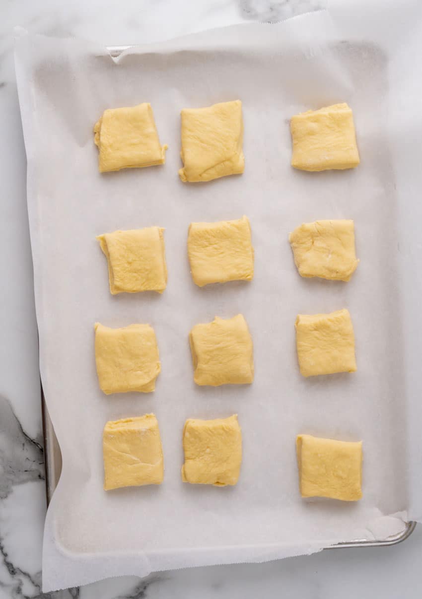 squares of texas roadhouse roll dough arranged in three rows on a parchment paper lined baking sheet