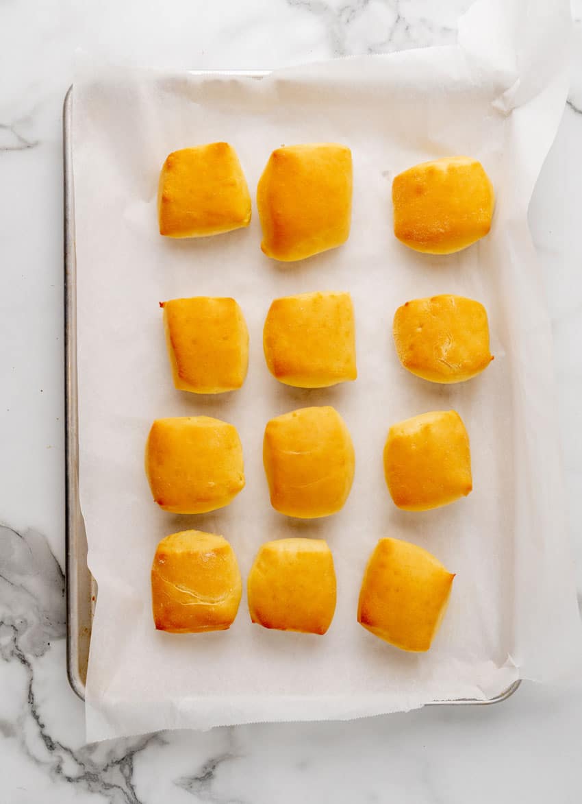 three rows of baked texas roadhouse rolls on a parchment paper lined baking sheet
