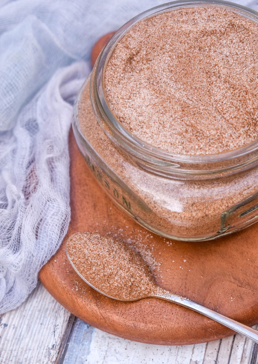 a silver spoon holding up a scoop of homemade cinnadust seasoning resting on a wooden coaster