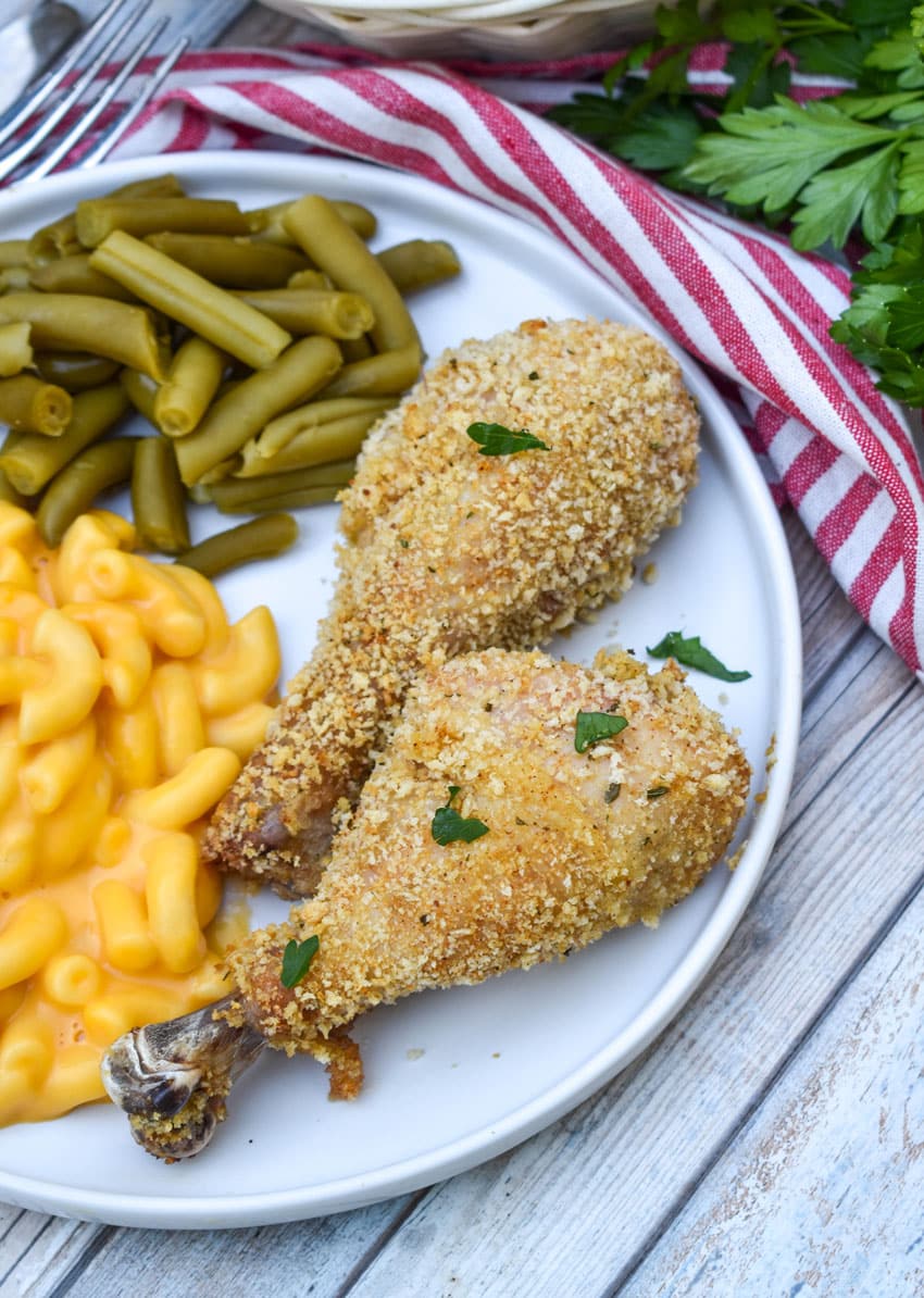 HOMEMADE SHAKE AND BAKE CHICKEN NEXT TO GREEN BEANS AND MACARONI & CHEESE ON A WHITE PLATE
