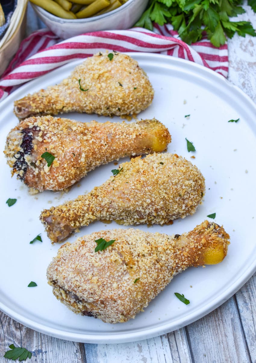 HOMEMADE SHAKE AND BAKE CHICKEN LEGS IN A ROW ON A WHITE SERIVNG PLATE