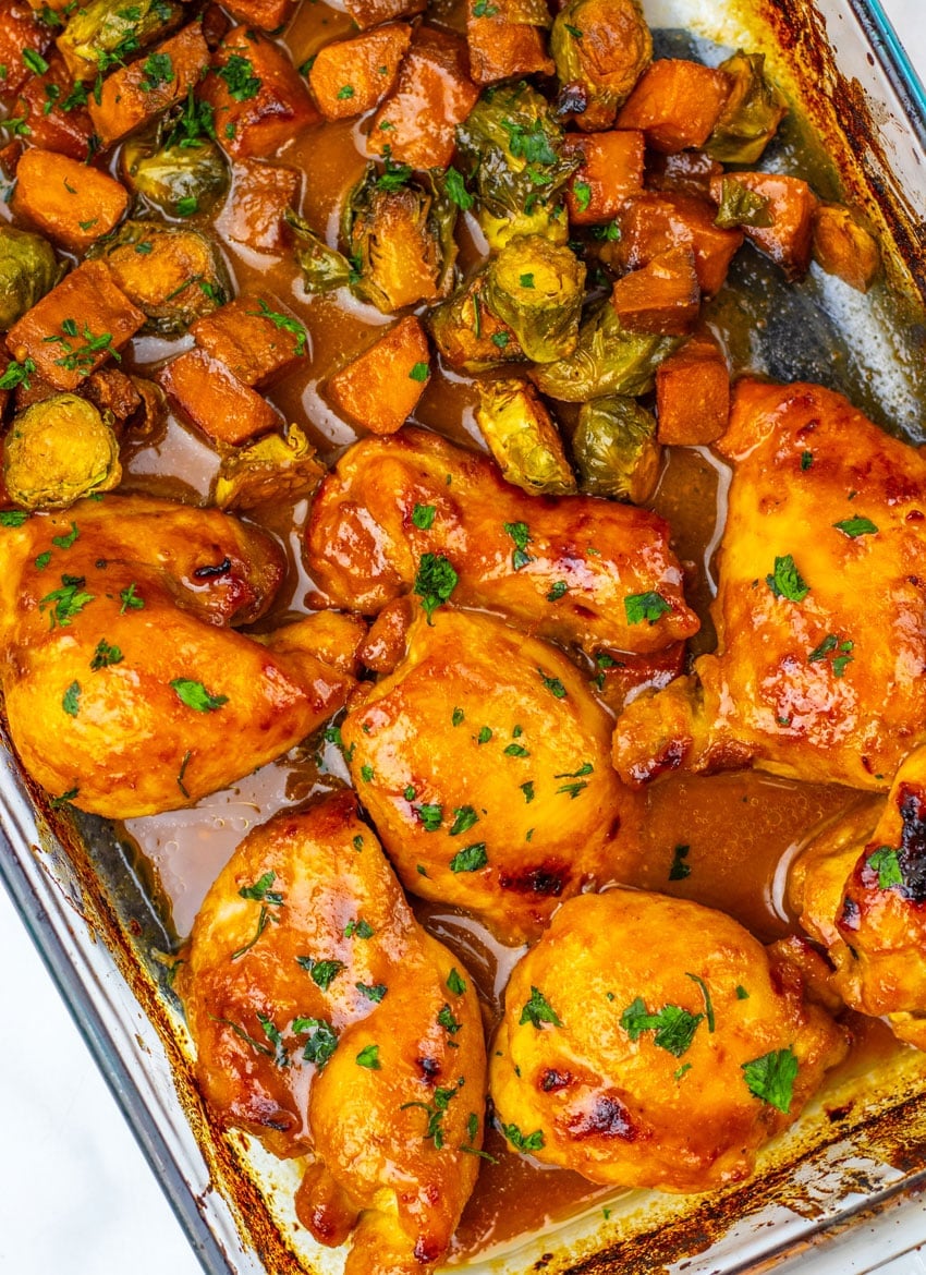 baked maple mustard chicken thighs and roasted vegetables in a glass baking dish