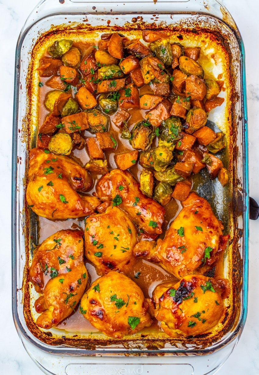 baked maple mustard chicken thighs and roasted vegetables in a glass baking dish