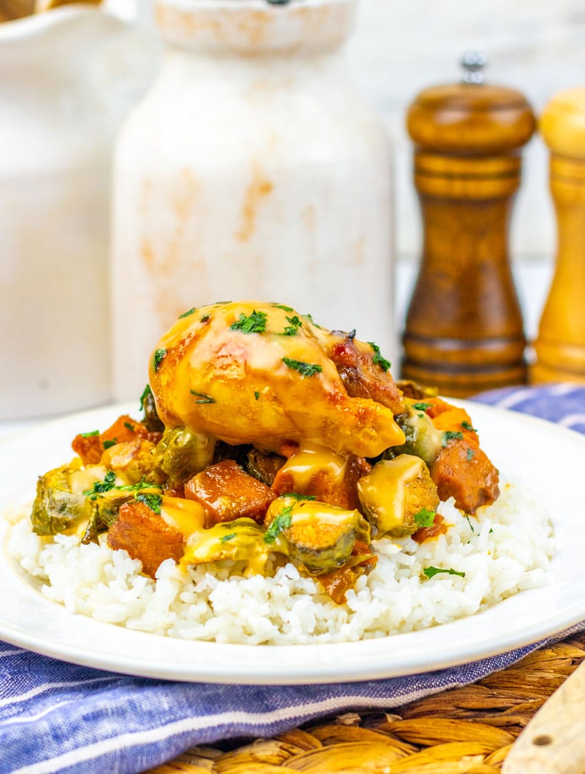 maple mustard chicken thighs and roasted vegetables over steamed rice on a white plate