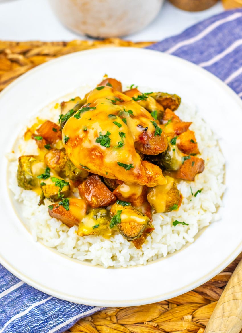 maple mustard chicken thighs and roasted vegetables over steamed rice on a white plate
