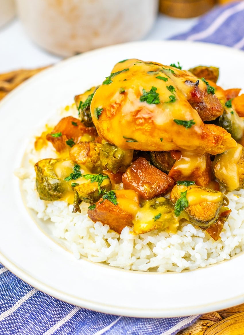 maple mustard chicken thighs and roasted vegetables over steamed rice on a white plate
