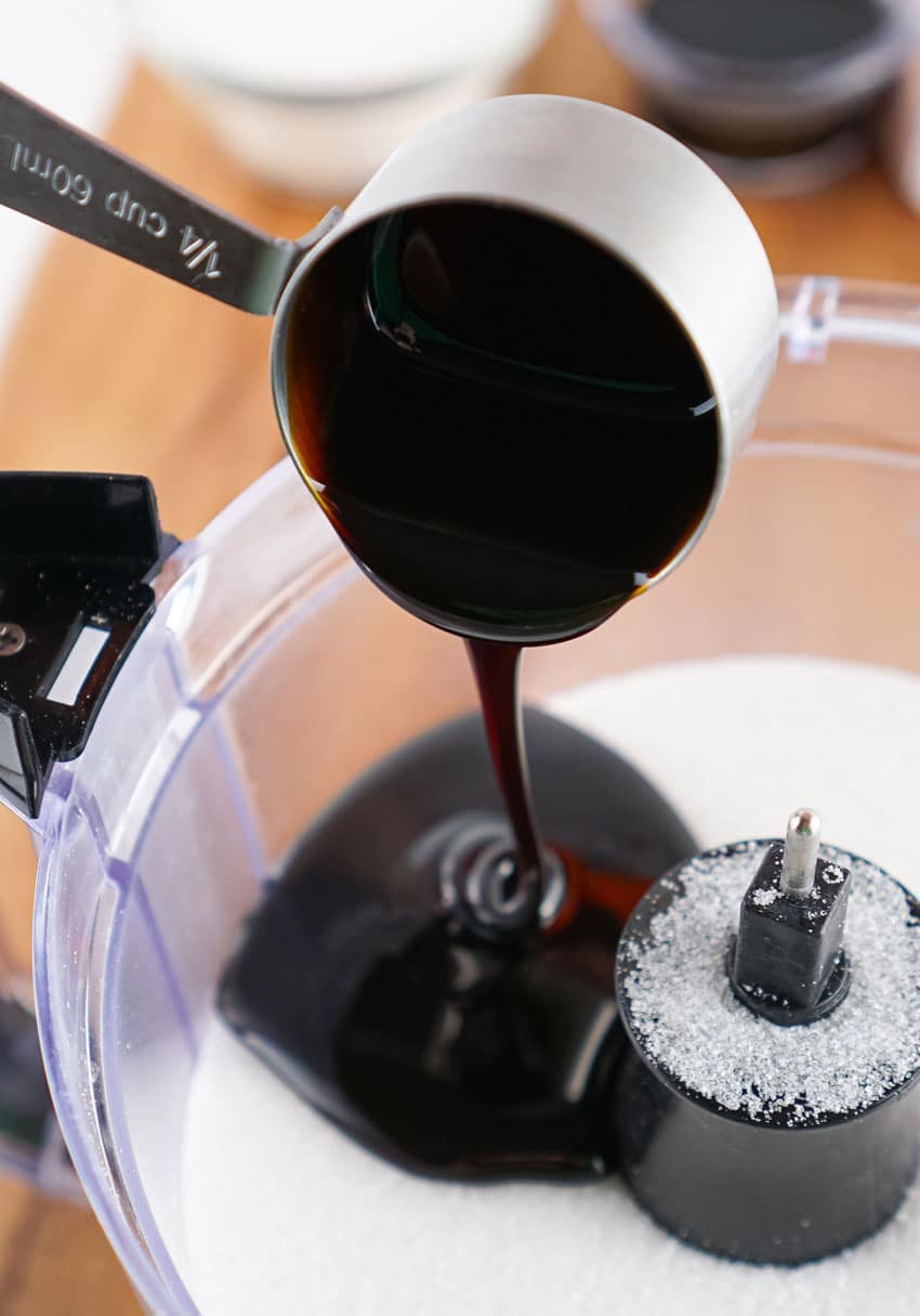 molasses being poured onto white sugar in a food processor