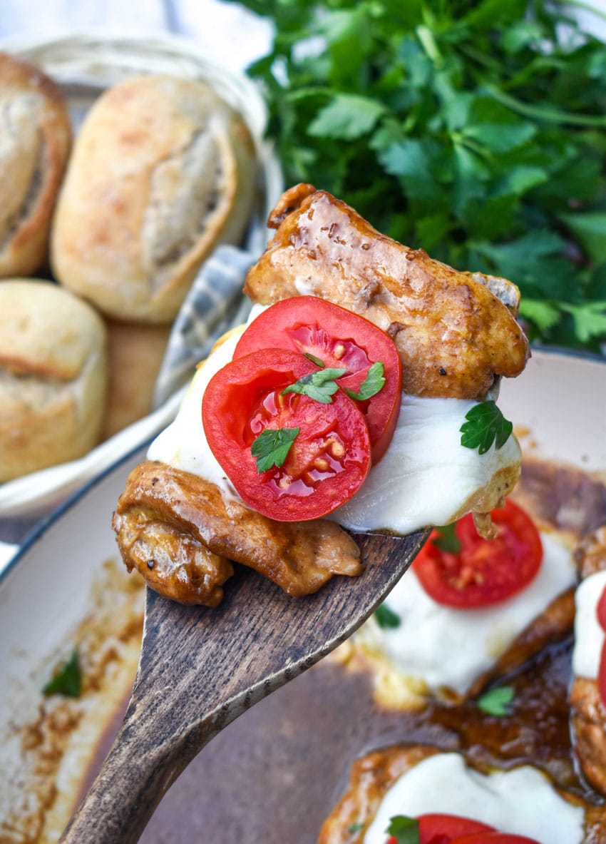 a wooden spatula holding up a slice of balsamic chicken with mozzarella