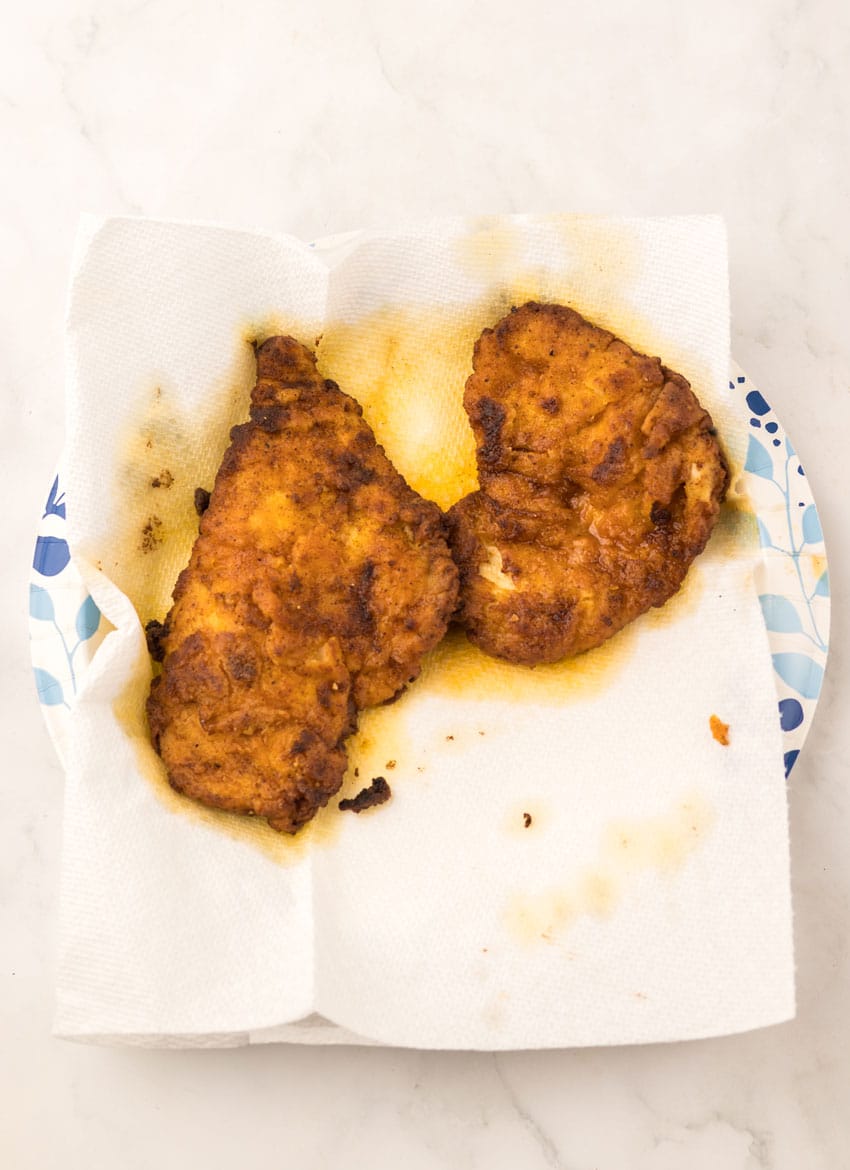 fried pieces of pickle juice marinated chicken drained on a paper towel lined paper plate