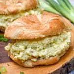 deviled egg salad on croissant rolls resting on a wooden cutting board